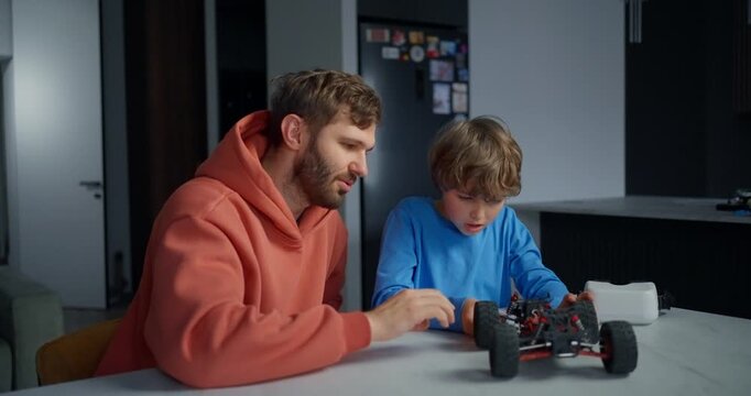 Father and young son assembling a small remote control car at a kitchen table, sharing hands-on learning, creativity, and family bonding at home