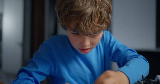 Child hands carefully assembling a remote control car chassis with exposed suspension, wires, gears and wheels on a tabletop workshop