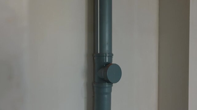 Gray drainage pipe mounted on interior wall close up