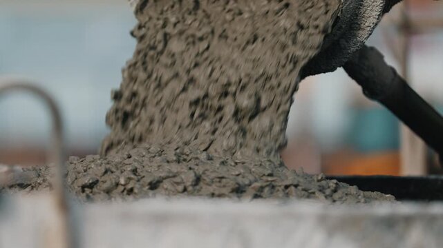 Pouring concrete from mixer chute into construction bucket close up