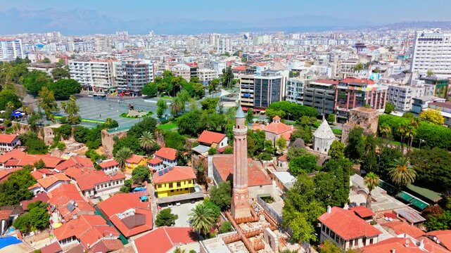 Drone view of Antalya, Turkey Yivli Minare Mosque and Old Town. Red rooftops, green trees and city skyline create a sunny historic travel scene.