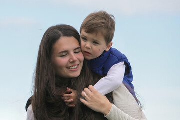 Fototapeta premium Closeup portrait of a toddler son affectionately hugging his smiling mother outdoors.