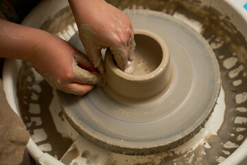 Fototapeta premium Artisan hands shaping wet clay on a pottery wheel in a workshop close up.