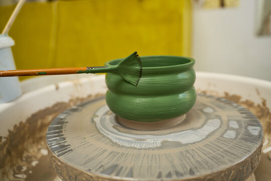 Potter using a wide brush to apply green underglaze to a large clay bowl.
