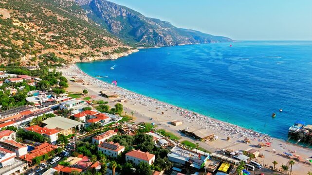Aerial view of Oludeniz Blue Lagoon, Turkey beach and sea. People relax under umbrellas, boats float nearby and paragliders fly above the sunny coast.