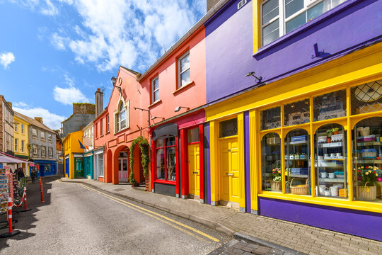 A narrow street of vibrant, multicolored storefronts in the historic center of Kinsale, a fishing port town in County Cork, Ireland.