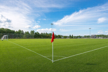Red corner flag standing on a green soccer field under a blue sky, empty football pitch for athletic competition and recreational sports training in a public park © Patrick
