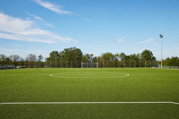 Empty soccer field with green artificial turf and white markings under a clear blue sky, professional football pitch for sports training, recreation and competition © Patrick
