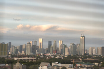 Fototapeta premium Golden light bathes urban Jakarta skyline at dusk. Tall buildings stretch upward into hazy sky.