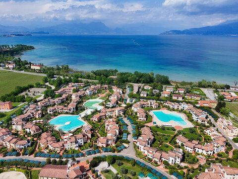 Aerial view of Lake Garda featuring luxury resort buildings with turquoise swimming pools and lush green landscapes Italy.