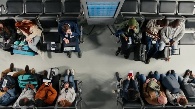 Top down view of upset passengers in airport make telephone calls home to tell bad news of being late after delayed flights. Frantic crowd reacts to flight cancellation red alert, high angle shot