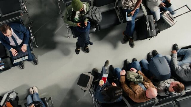 Multiethnic travelers in airport hub going to boarding gate, carrying wheeled luggage. Diverse people in airport lounge standing up from metal benches, preparing for boarding call