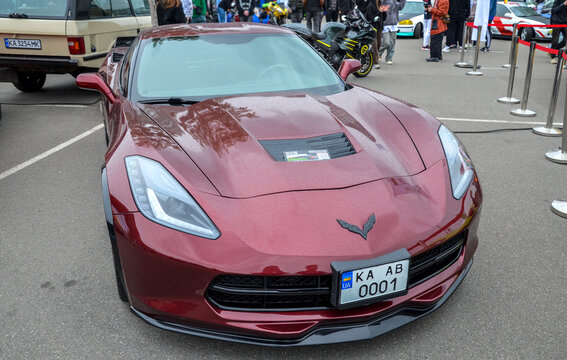 Luxury maroon American sports car Chevrolet Corvette C7 features distinctive carbon fiber hood vent, modern LED headlights, and aggressive front aerodynamic splitter