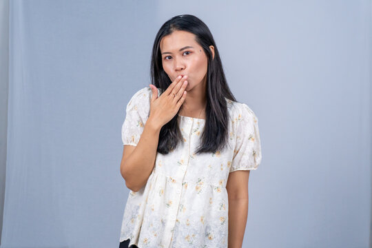 Young Asian woman in white floral blouse covering mouth with hand, shocked or surprised