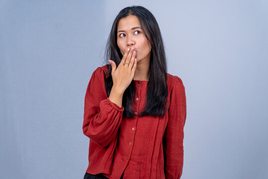 Surprised Young Asian woman in red shirt covering mouth with hand, isolated grey background