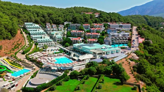 Drone view of Oludeniz, Turkey resort in green hills. Pool, hotel buildings, forested mountains and sunny valley create a summer vacation scene.
