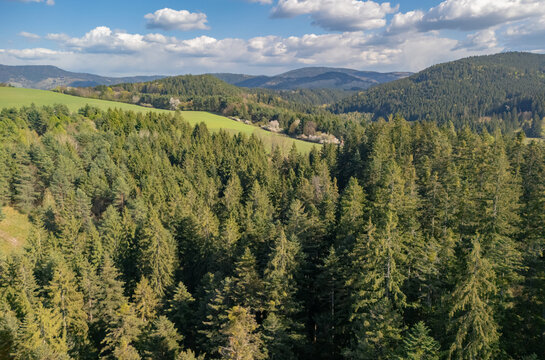 Aerial view of the Driekyna valley featuring dense evergreen forests and rolling green hills under a blue sky with scattered clouds in Slovenska Lupca, Banskobystricky kraj, Slovakia.