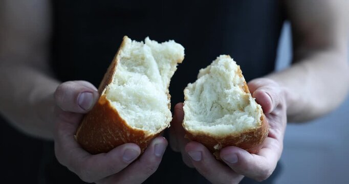 Man breaking loaf of fresh bread indoors, closeup