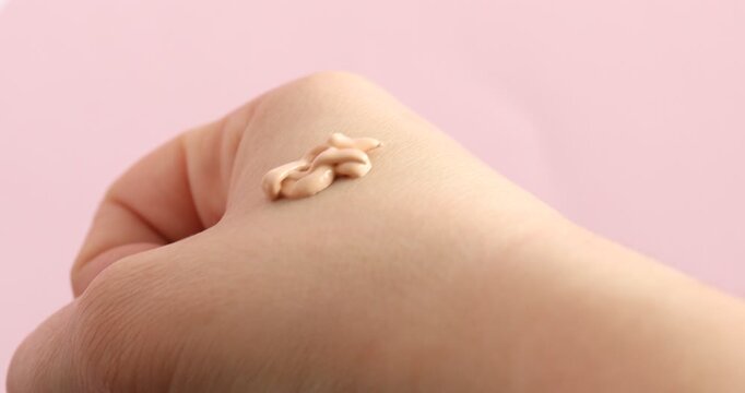Woman applying skin foundation onto her hand on pink background, closeup