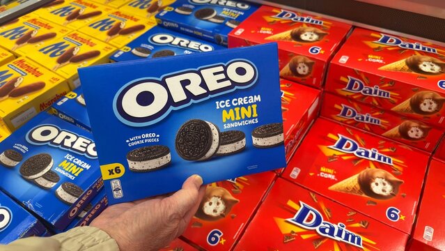 Hand holding a blue box of ice cream mini sandwiches featuring Oreo cookies in Swedish grocery store aisle with colorful packaging of other products in the background