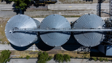 Vertical top-down aerial view of three metal grain silos and conveyor bridge © Amatis Art