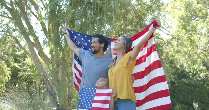 Family posing in garden, adults lifting arms raising US flag, child holding small flag for portrait