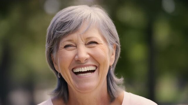 Elderly woman with gray hair laughing heartily with her eyes closed outdoors