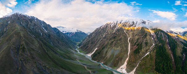 The onset of summer in the high mountains, aerial panoramic view of a remote alpine valley with parallel leading lines created by a winding glacial river and a mountain trail © asif