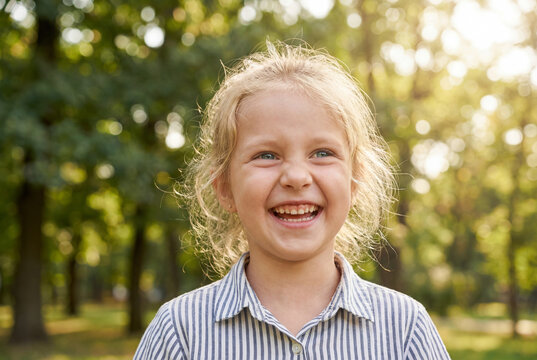 Happy young girl giggling delightfully in a sunny park outdoors