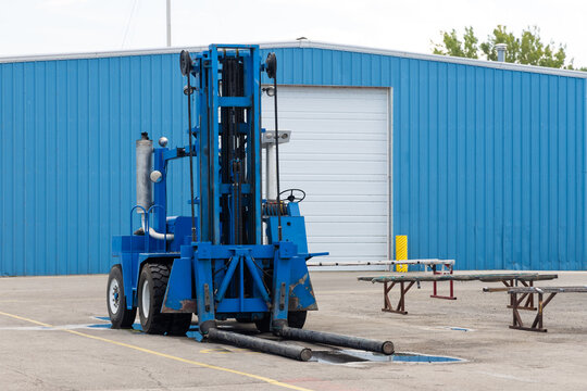 Blue forklift with long forks parked outside warehouse