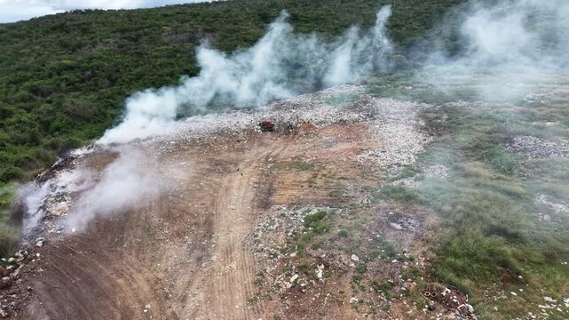 Lix&atilde;o a c&eacute;u aberto com fuma&ccedil;a t&oacute;xica e degradante impacto ambiental. Vista panor&acirc;mica de aterro sanit&aacute;rio irregular (lix&atilde;o) liberando fuma&ccedil;a no meio da vegeta&ccedil;&atilde;o. lixo se acumula, causando polui&ccedil;&atilde;o.