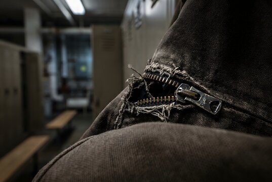 Foreground blur macro of a canvas work jacket with a broken metal zipper and torn fabric