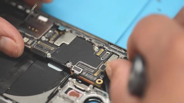Technician repairing disassembled smartphone motherboard in professional electronics workshop