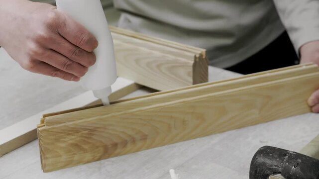 Close up of worker applying glue into wooden joints during furniture assembly in woodworking factory.