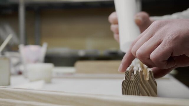 Close up of worker applying adhesive into wooden joints during furniture manufacturing process.