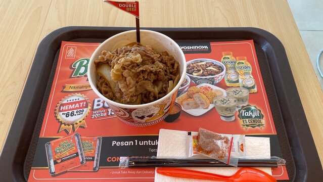 Yoshinoya Japanese Restaurant beef bowl meal with double beef toppings and traditional chili seasoning served on a paper tray mat in Kuta - Bali, Indonesia, March 29, 2023