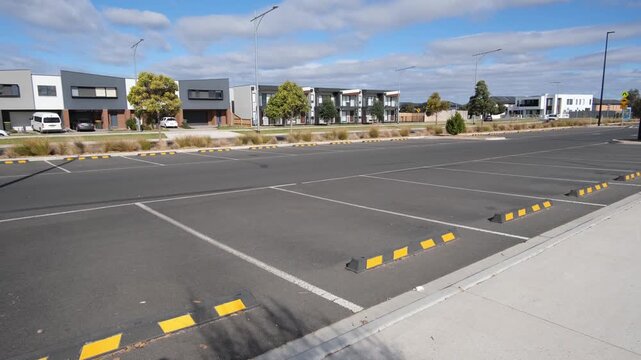 Newly constructed suburban public car park in Truganina, Melbourne, Australia, featuring marked parking bays, wheel stops,&nbsp;with modern residential townhouses nearby.