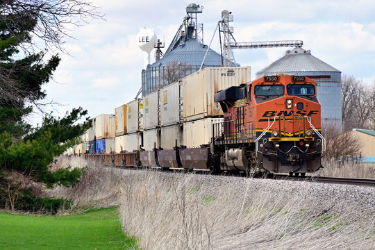 A Burlington Northern Santa Fe locomotive serves as a rear-train distributed power unit (DPU) on a westbound intermodal freight train passing grain elevators at an Illinois farmers cooperative