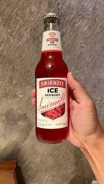 Smirnoff Ice Raspberry vodka mixed drink bottle held by person against a grey textured wall background at a resort in Kuta Selatan - Bali, Indonesia, March 27, 2023