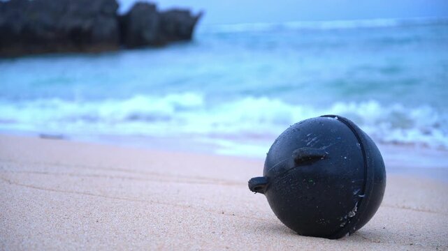 砂浜に打ち上げられた黒いプラスチックの浮きとボケた波打ち際（海洋ゴミ・SDGs）