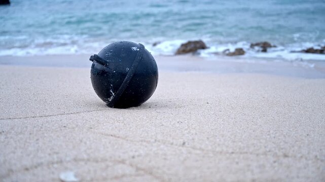 砂浜に打ち上げられた黒いプラスチックの浮きとボケた波打ち際（海洋ゴミ・SDGs）