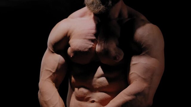 A male bodybuilder poses in shorts, showing off his muscles. Close-up of his chest and abs.