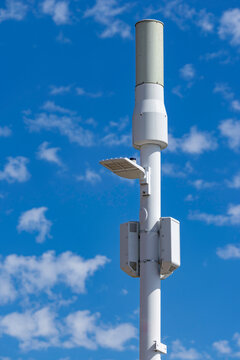 Modern 5G small cell telecommunications antenna and LED street light mounted on a white smart pole against a blue sky, USA