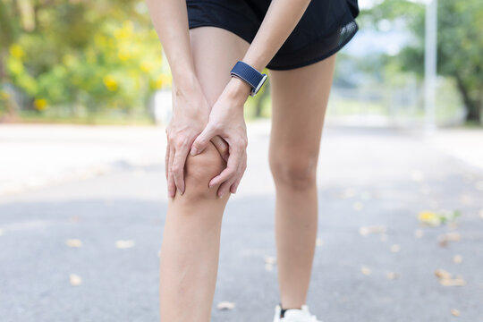 Female runner holding her knee experiencing severe pain and physical discomfort after an outdoor injury stopping on road touching hurting leg joint showing suffering during an exercise routine