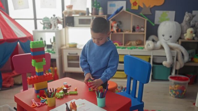 Boy stacking colorful blocks with hands at preschool building table; concentration imaginative play.