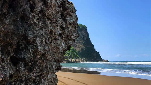 Tropical beach landscape with turquoise water and majestic cliffs viewed from a rocky shoreline. Scenic coast travel destination in summer season. Parangtritis, Yogyakarta, Indonesia