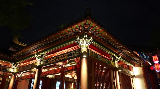 Night view of traditional Chinese architecture featuring ornate eaves, dougong brackets, and colorful painted details illuminated by warm lighting