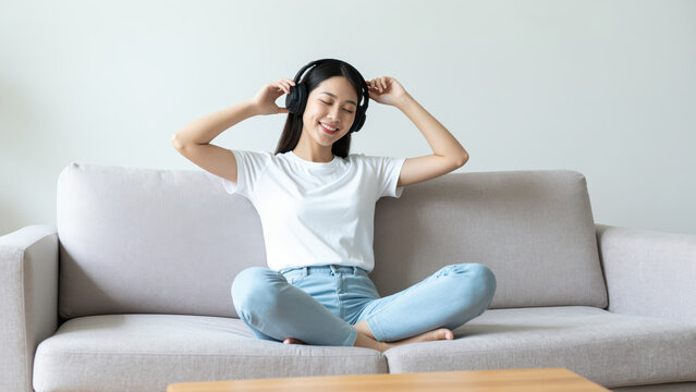 Serene Listening on the Sofa: A young individual finds solace and enjoyment in music, relaxing on the couch with a pair of headphones. Capturing a moment of pure contentment and auditory bliss.