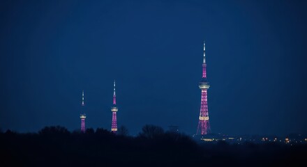 Fototapeta premium Distant towers illuminated with purple lights against a deep blue night sky, showcasing city infrastructure and urban beauty.