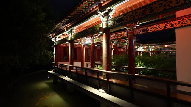 Traditional Chinese corridor bridge and waterside pavilion at night with illuminated eaves and reflections in the pond